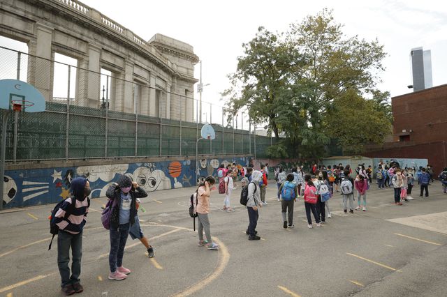 Children stand in a playground waiting to be allowed into school near the Manhattan Bridge.